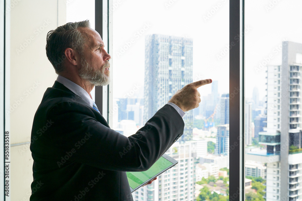 Smart Businessman hold tablet and point finger to outsite the window for forecast business trend and cityscape view Smart Businessman hold tablet and point finger to outsite the window for forecast business trend and cityscape view