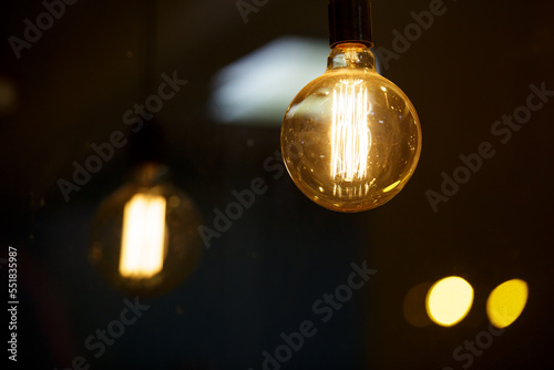 A burning light bulb glows faintly against the background of blurry yellow lights. Energy crisis. Blackout.