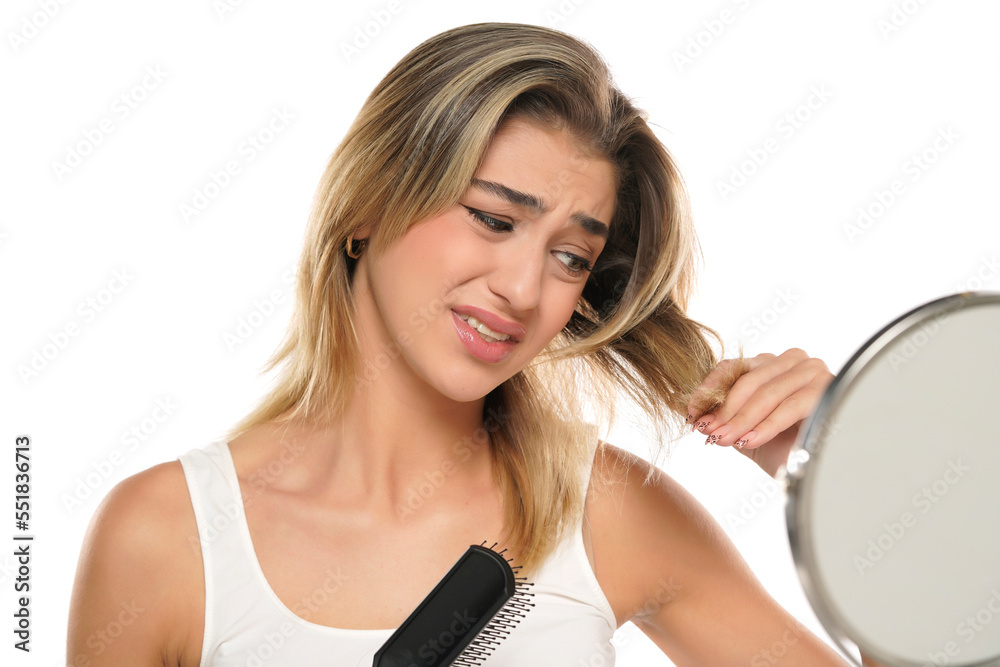 Young nervous unhappy woman brushing hair in front of a mirror on a white background Young nervous unhappy woman brushing hair in front of a mirror on a white background