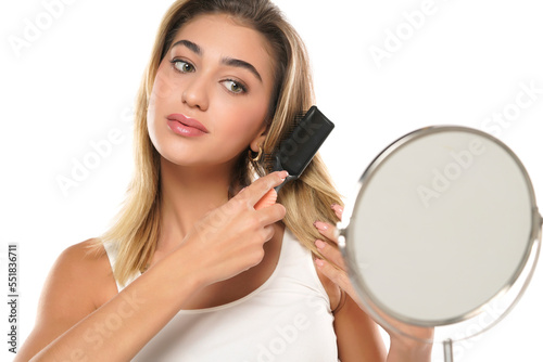 Young woman brushing healthy hair in front of a mirror on a white background