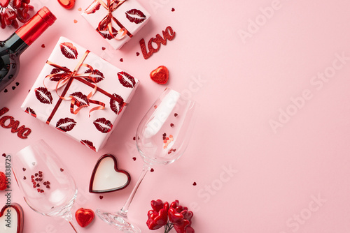 Valentine's Day concept. Top view photo of gift boxes wine bottle glasses with confetti heart shaped chocolate candies candles and inscriptions love on isolated light pink background with copyspace