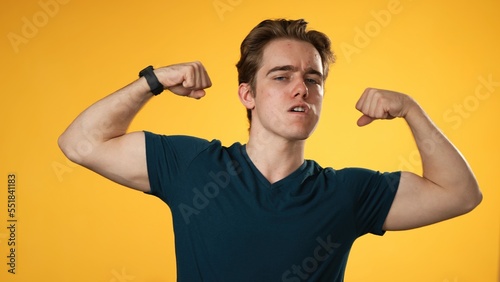 Portrait of young hipster man 20s with show muscles, have fun energy isolated on yellow background in studio