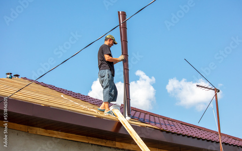 Workers install metal roofing on the wooden roof of a house.