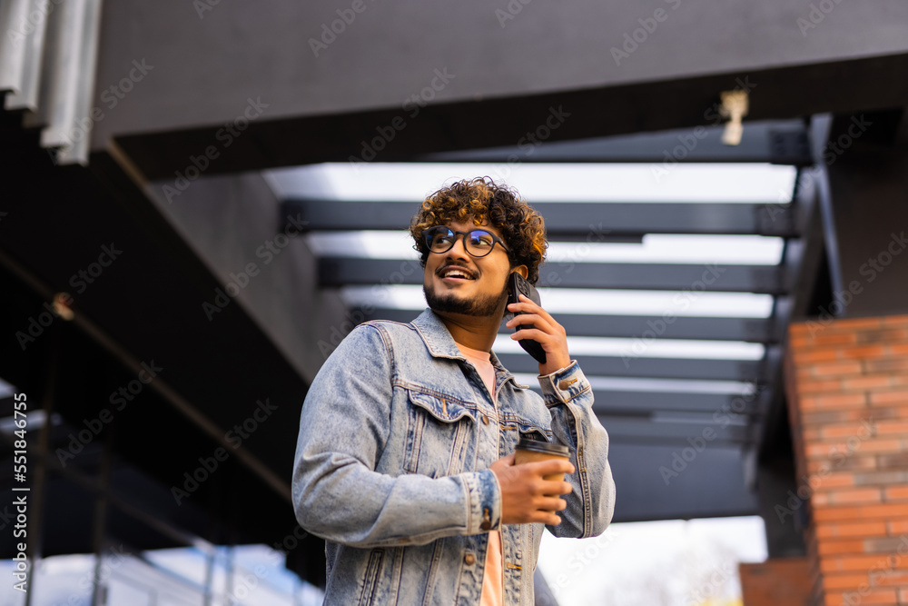 Fototapeta premium Handsome smiling young man dressed casually spending time outdoors at the city, talk mobile phone while walking down stairs