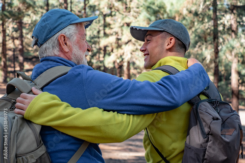 Back view of smiling beautiful couple of grandfather and young grandson walking together embracing each other in the forest enjoying free time and nature. Adventureisageless © luciano