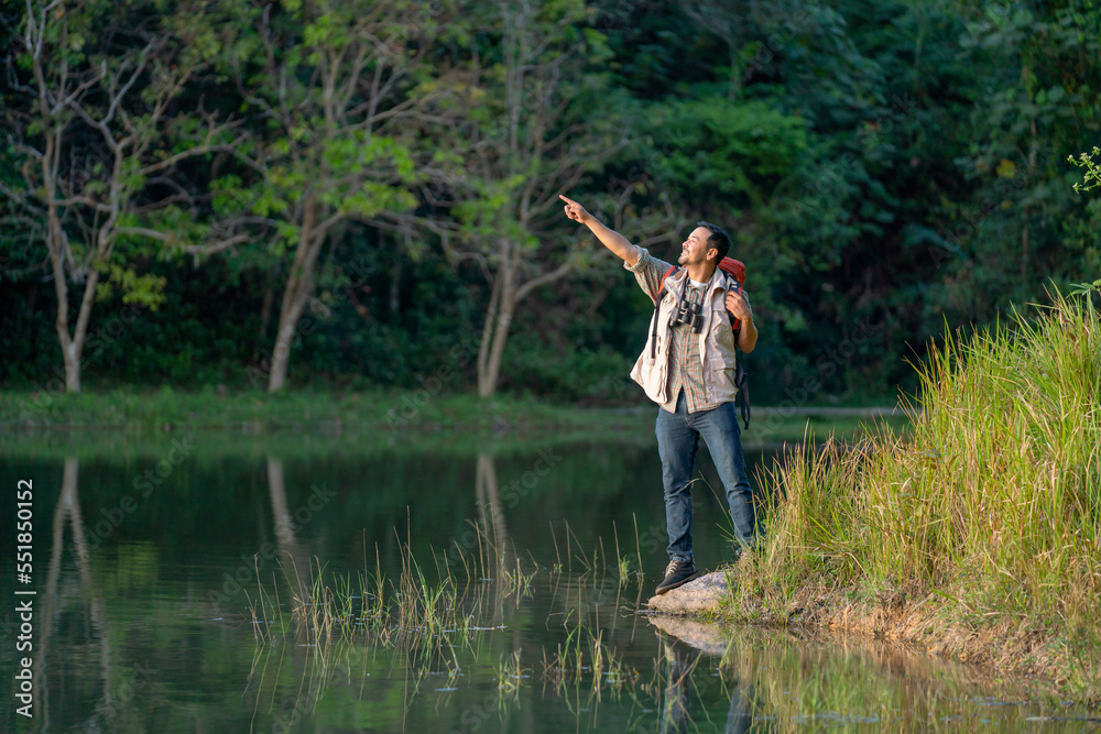 Asian man stand near lake in national park and point to the left and he look happy during travel and camping in national park. Asian man stand near lake in national park and point to the left and he look happy during travel and camping in national park.