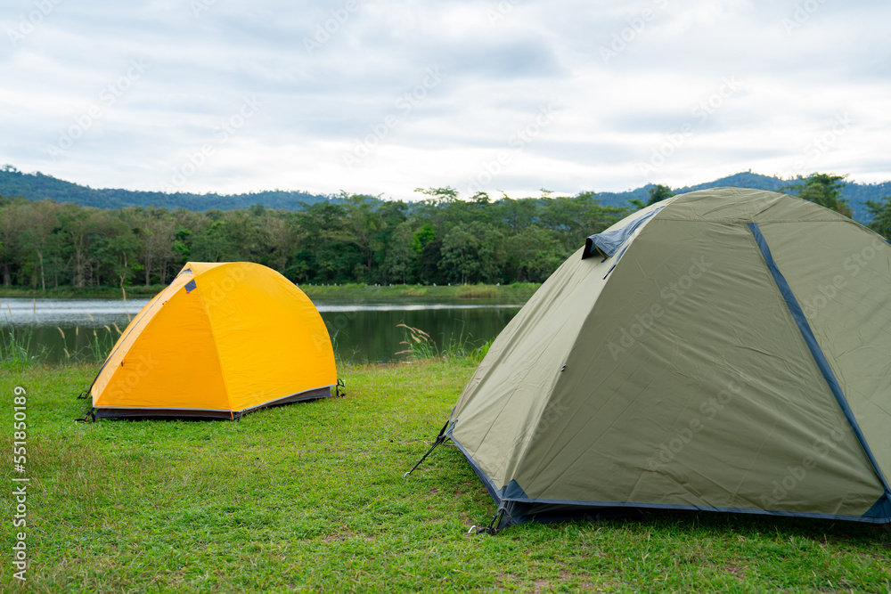 Yellow and grey green tent are set on grass field or meadow near lake with cloudy sky and it look peaceful and quiet place for people who want to rest and relax.