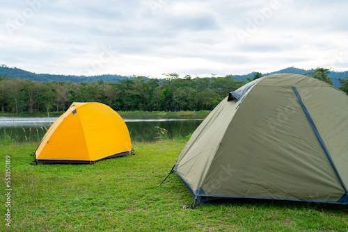 Yellow and grey green tent are set on grass field or meadow near lake with cloudy sky and it look peaceful and quiet place for people who want to rest and relax.