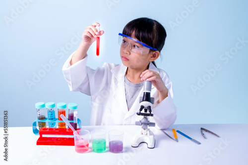 Little asian cute girl 7 years old role playing a scientist in science lab with equipment and looking at liquid chemicals in tubes.