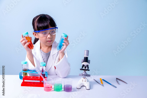 Little cute girl learning a scientist in biology lab with equipment and looking at liquid chemicals in tube. Learning and education of kid.