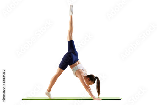 Portrait of young sportive woman training, doing stretching exercises, rising leg up, body down isolated over white background. Concept of sport, fitness, health
