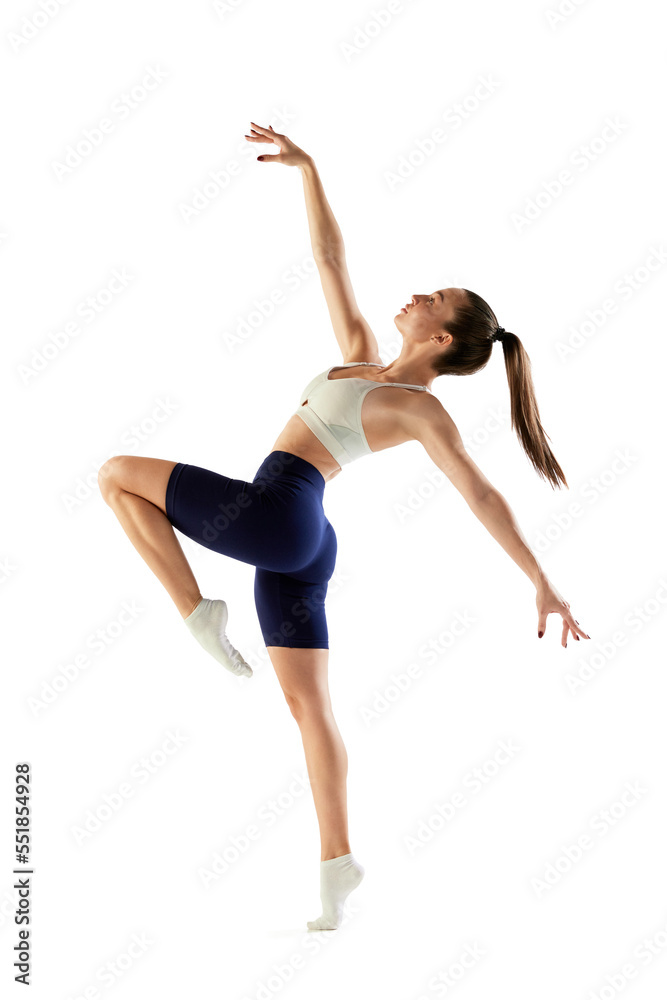 Portrait of young sportive woman training, doing full body exercises, standing on tiptoe isolated over white background. Concept of sport, fitness, health