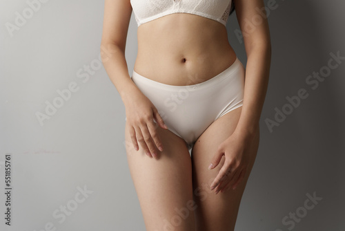 Close up asian female body wearing white high-waist panties over grey background.