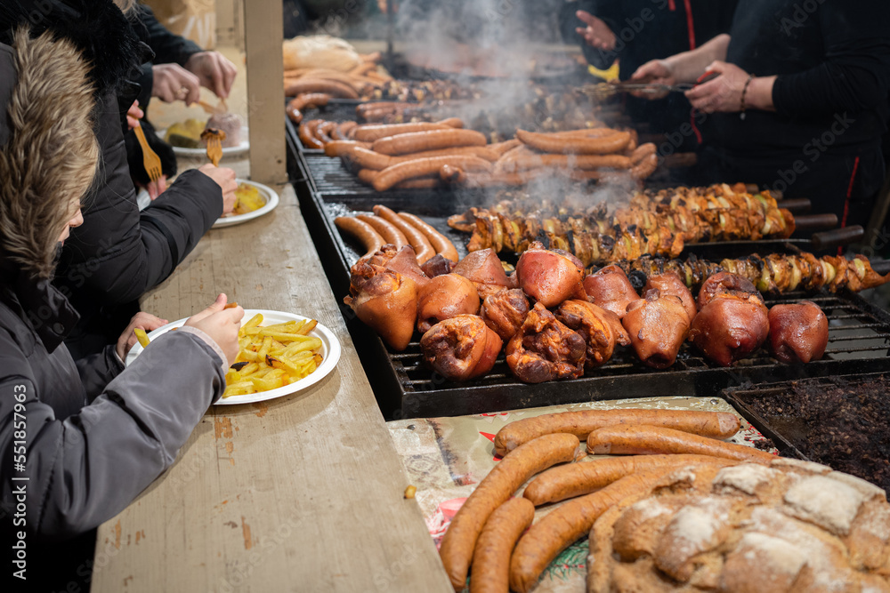 Stand with roasted meat including pork knuckle, and sausages on the grill during the Christmas market