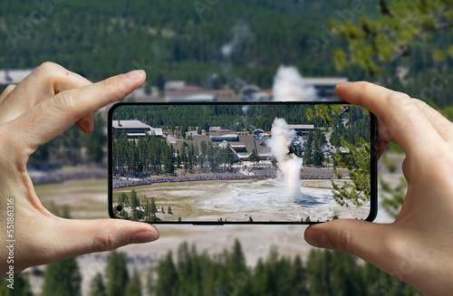 фотографія Tourist taking a picture of the erupting geyser old faithful at the Yellowstone national park, USA