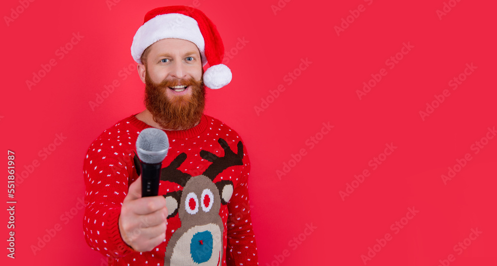 Happy bearded man in Christmas wear giving microphone studio isolated on red