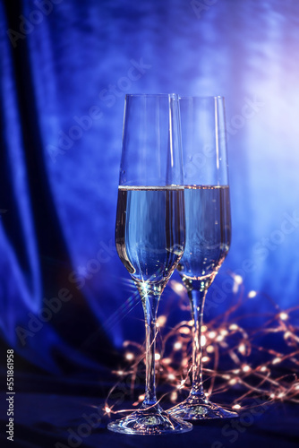 Glasses of champagne and a golden light garland on a blue velvet background. Christmas and New Year event concept. Holiday postcard