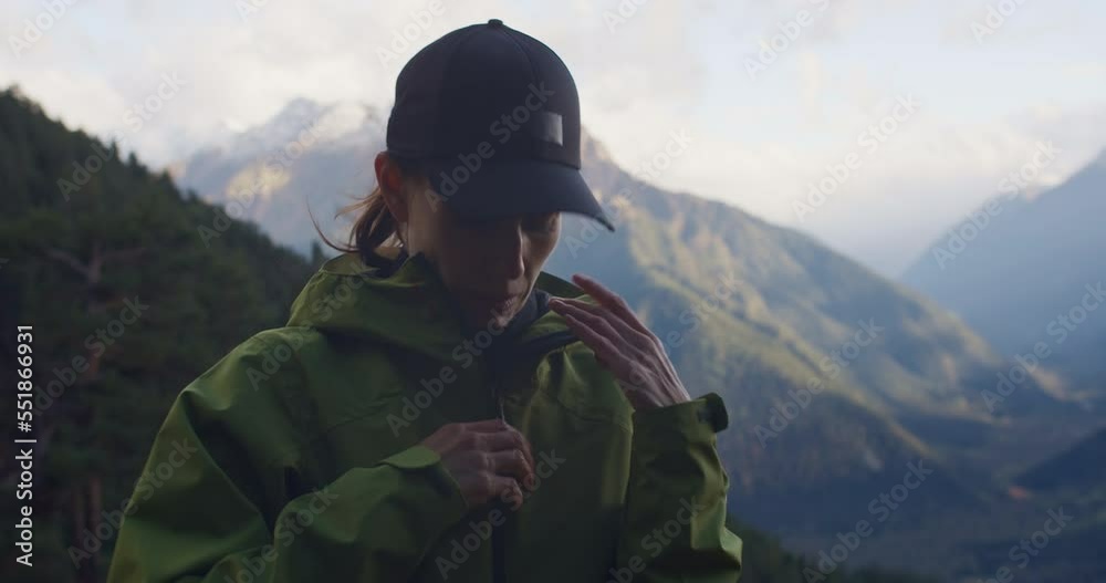 Hiker woman rub hands and put on hood for warming in trekking in mountain. medium shot Hiker woman rub hands and put on hood for warming in trekking in mountain. medium shot