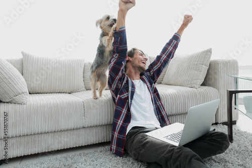 happy guy exults with his dog sitting near the sofa in the living room.