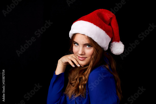 caucasian girl with long hair in blue dress wearing santa claus hat isolated on black background