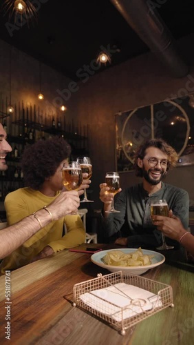 Vertical video of a A group of colleague workers toast with beer in the restaurant bar after work at the pub happy hour. Happy friends having fun together drinking alcohol indoors. photo