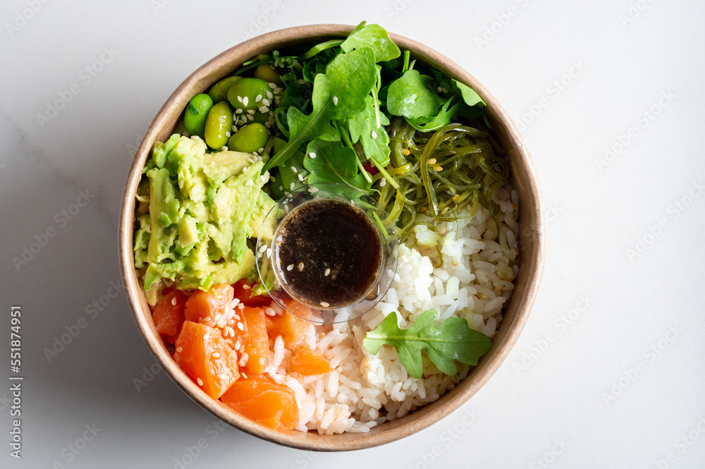 Poke bowl with sushi rice, raw salmon, avocado, seaweed salad, rocket