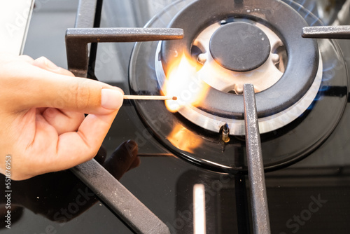 Hand with a match turns on the gas burner on the gas stove.