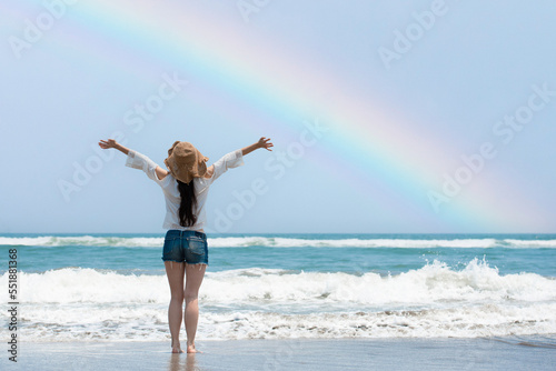 虹の出たビーチで両手を広げる女性