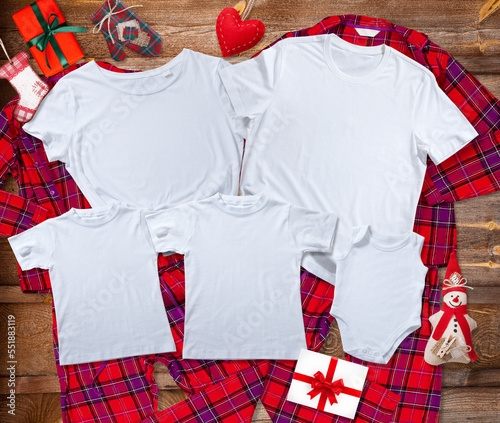 Blank white t-shirts for the whole family on the background of bright pajamas on a wooden background with Christmas presents
