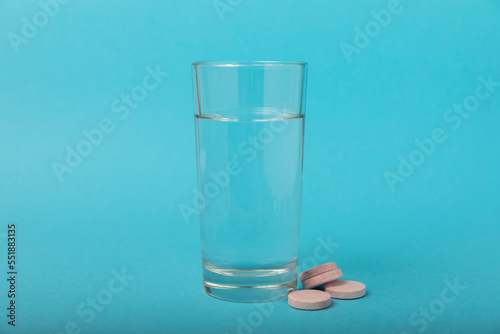 An effervescent vitamin tablet drops and dissolves in a glass of water on a blue background. The concept of health. Medicine concept. Place for text.