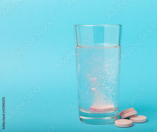 An effervescent vitamin tablet drops and dissolves in a glass of water on a blue background. The concept of health. Medicine concept. Place for text.