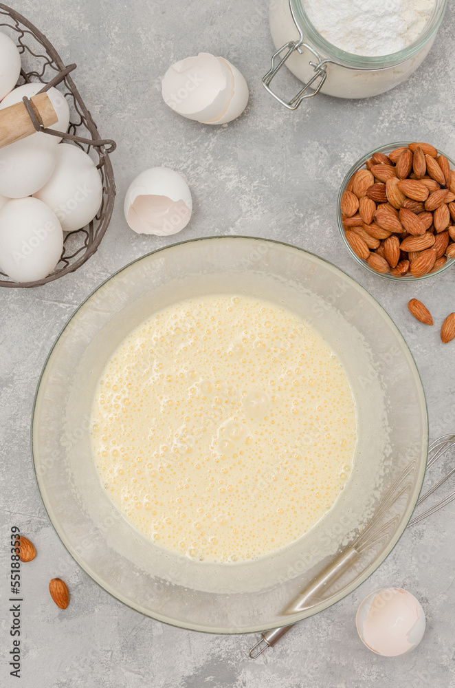 Recipe step by step. The process of making Italian cantucini cookies. Whipped eggs with sugar in a bowl on a gray concrete background. Top view. Recipe step by step. The process of making Italian cantucini cookies. Whipped eggs with sugar in a bowl on a gray concrete background. Top view.