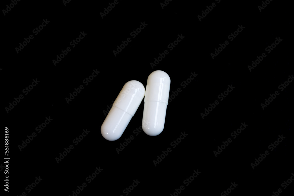 Two white capsule pills on black background isolated object. Two white capsule pills on black background isolated object.