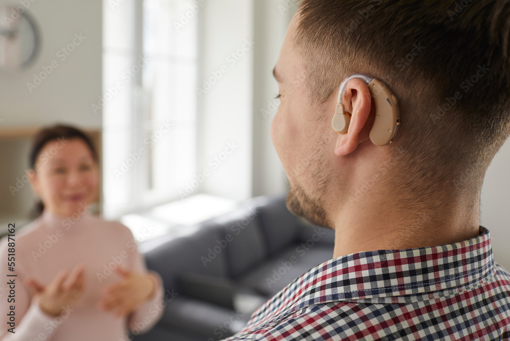 Hearing-impaired man uses modern model of hearing aid that is inserted into his ear. Close up of hearing aid on man's ear as he looks at woman who communicates with him using sign language. Hearing-impaired man uses modern model of hearing aid that is inserted into his ear. Close up of hearing aid on man's ear as he looks at woman who communicates with him using sign language.