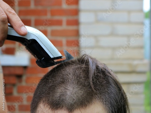 cutting long hair with a trimmer for a teenager or a young man at home, a simple short men's haircut for a minimal nozzle on a clipper, shaving a man's head with a trimmer baldly photo