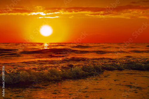 The sun is sinking into the sea. The sun s rays pass through the waves  smoothly rolling over each other. A bright orange sunset over the sea is large.the concept of a romantic summer vacation.tourism