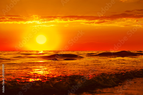 The sun is sinking into the sea. The sun's rays pass through the waves, smoothly rolling onto the shore. A bright orange sunset over the sea is magnificent. the concept of a romantic summer vacation. © Viktorya 