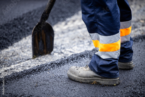 Road construction or reparation and worker with shovel spreading new layer of asphalt.