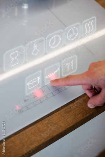 A man's hand programs his stove with the smart kitchen app futuristic interface in the kitchen