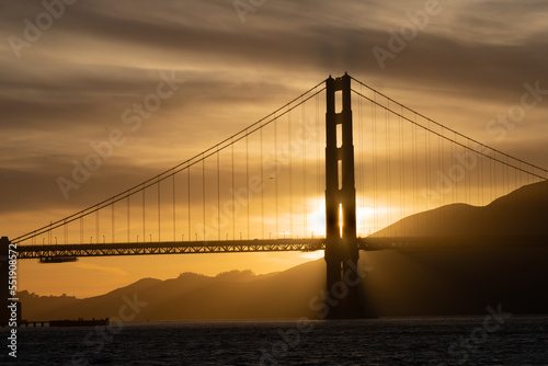 Golden gate bridge at sunset with a yellow., gold, brown and black sky and Marin County shown to the right. 