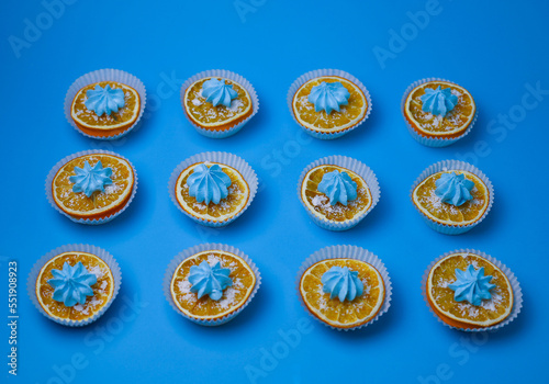 bright sweet delicious orange oranges in white muffin tins sprinkled with white powder and decorated with blue mini cakes on a bright blue background. for menu signage labels for cookbook splash scree