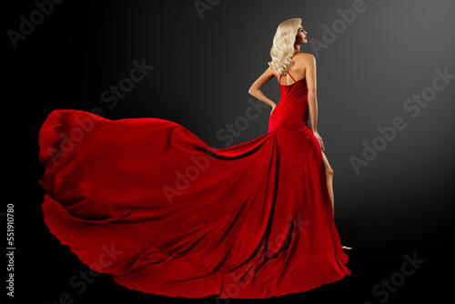 Fashion Woman in Red Dress with Long Train over Black. Sexy Blond Hair Girl in Evening Silk Gown Back Side View. Beautiful Model Profile with Curly Hairstyle over Dark Gray Background