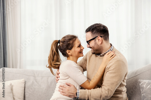 A happy couple is hugging in a living room and looking at each other.