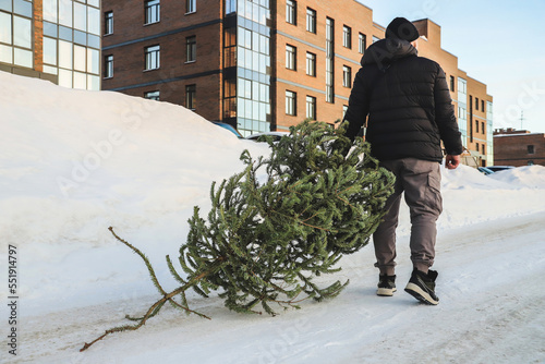 A man drags an used Christmas tree to the dumpster. After Christmas. Snowy winter. Outdoors. Selective focus photo