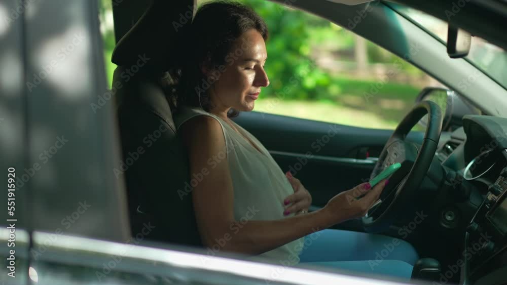 Happy pregnant woman messaging online in smartphone application sitting on driver's seat in vehicle. Side view portrait of confident beautiful Caucasian lady in car on sunny day outdoors. Slow motion Happy pregnant woman messaging online in smartphone application sitting on driver's seat in vehicle. Side view portrait of confident beautiful Caucasian lady in car on sunny day outdoors. Slow motion