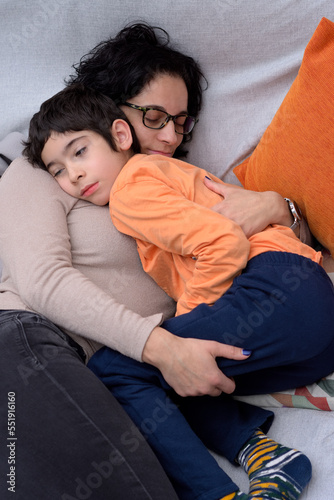 A young mother hugging very lovingly and tenderly her son, both of them are lying on the sofa. Close-up photograph, vertical format. Photograph with space for copy space