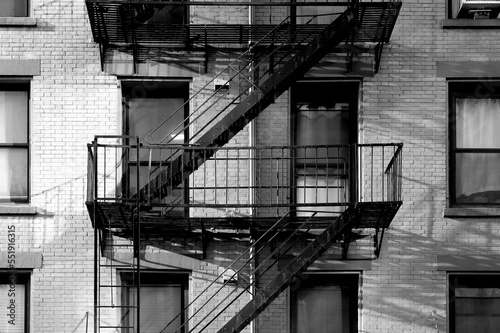 black and white close up New York City apartment building with brick exterior, windows, and diagonal fire escape stairs