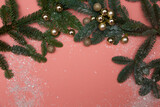 Green branches of a Christmas tree with artificial snow decorated with golden Christmas balls on a pink background top view