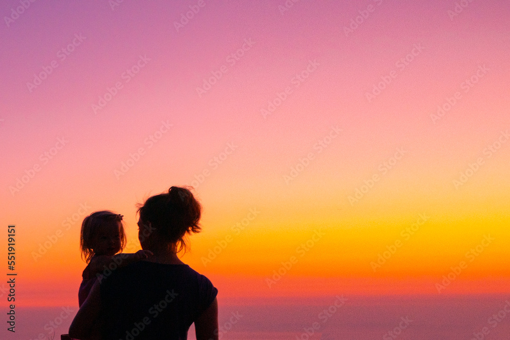 Silhouettes on a gradient sky. Mom and daughter are standing at sunset. Beautiful picture of motherhood