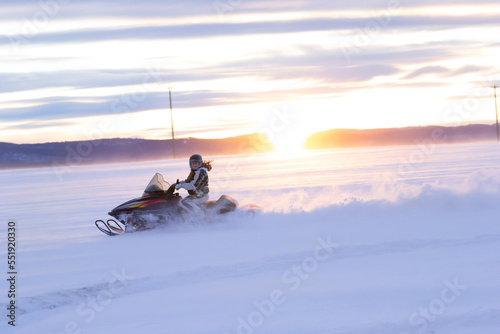 Female rider is drifting on skidoo on the winter snowy field.